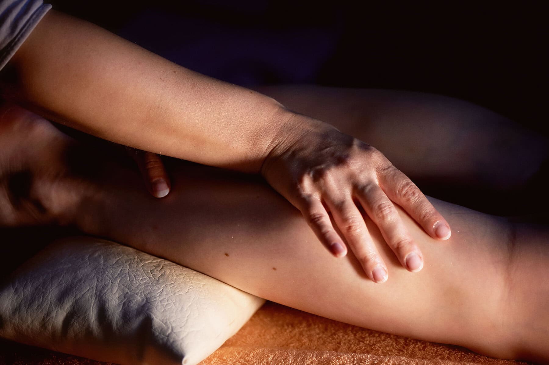 Sesame oil massage for calf muscle. Relaxation treatment for young female, close up. Sports massage - Leg massage - Physical therapist doing massage of calfs, applying strong finger pressure. Toned image, selective focus. Horizontal view of masseur massaging female calf