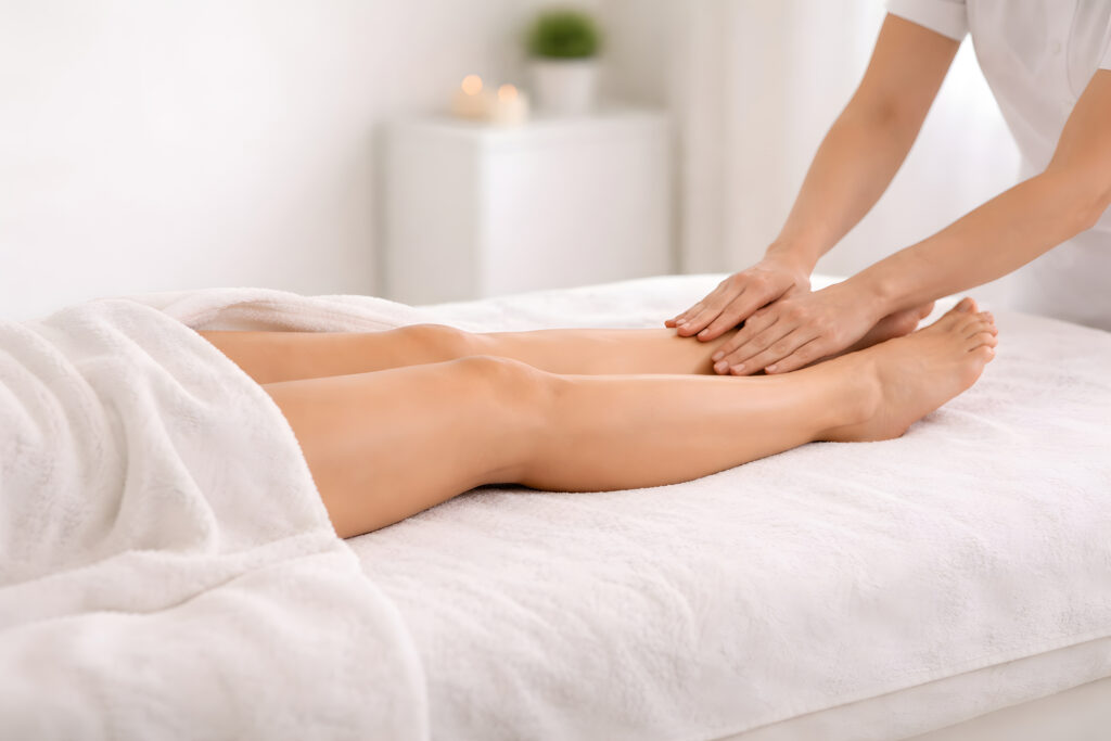 Hands apply gentle manual lymphatic drainage on client legs during a wellness therapy session for swelling reduction and recovery